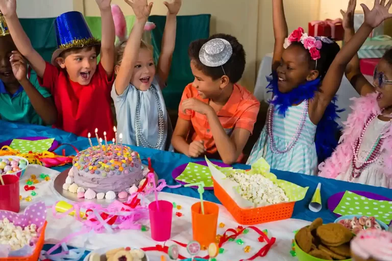 Un grupo de niños y niñas celebran una fiesta de cumpleaños. Sobre la mesa hay una tarta con siete velas