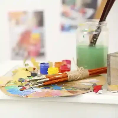 Una mesa con una paleta de pintor y varios pinceles manchados de pintura de colores, en una clase de dibujo y pintura.