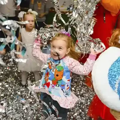 Una niña se divierte con serpentinas en una fiesta infantil de cumpleaños, mientras otra niña le observa desde detrás.