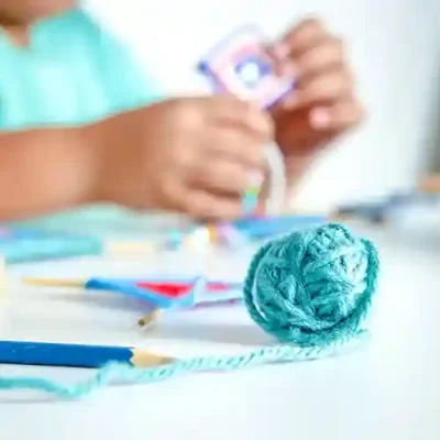 Un niño construye una cometa en miniatura en una clase de manualidades en inglés. Delante hay un ovillo de lana azul, otra cometa en miniatura y un lápiz.