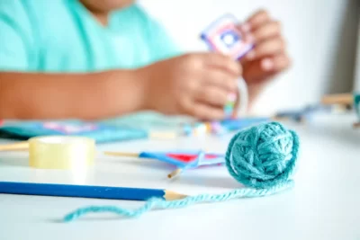 Un niño construye una cometa en miniatura en una clase de manualidades en inglés. Delante hay un ovillo de lana azul, otra cometa en miniatura y un lápiz.
